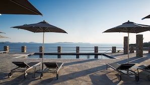 A poolside area with lounge chairs and umbrellas, overlooking a body of water and distant mountains.