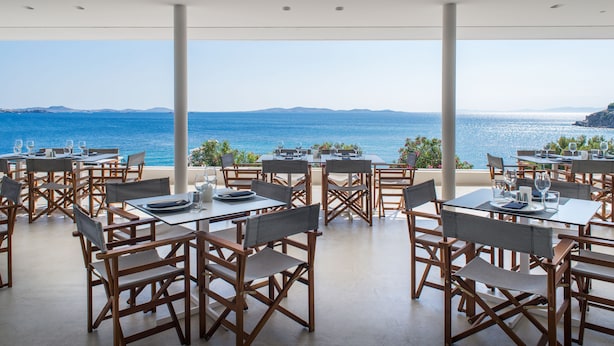 An outdoor dining area with tables and chairs, overlooking a body of water and distant land.