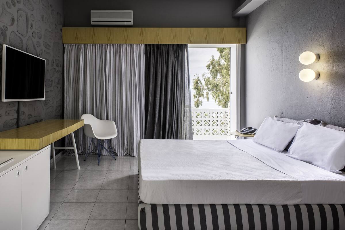 Une chambre d’hôtel moderne équipée d’un lit, d’un bureau, d’une chaise, d’une télévision et d’un balcon avec des rideaux.