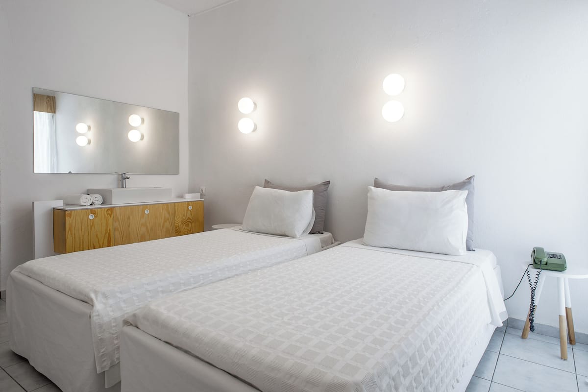 A hotel room with two beds, a wooden dresser, a mirror with lights, and a bedside table with a phone.