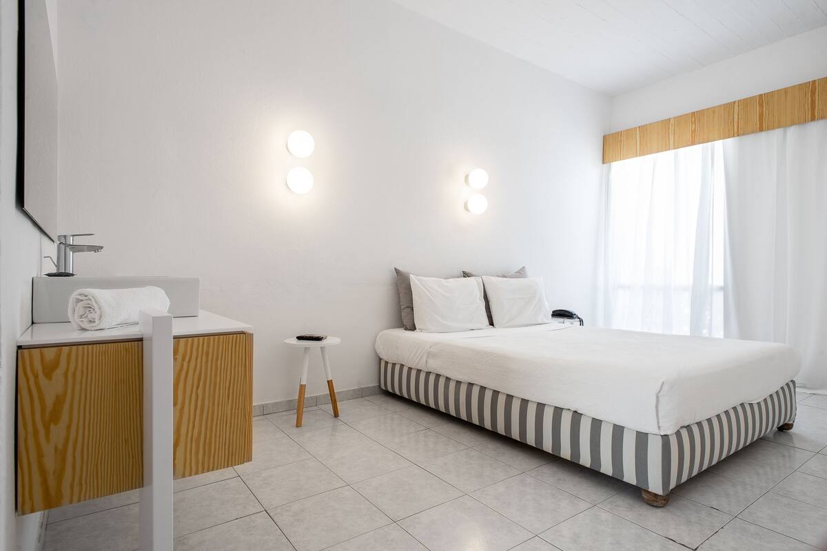 Une chambre d’hôtel moderne, équipée d’un lit, d’une petite coiffeuse en bois et d’une table de chevet.