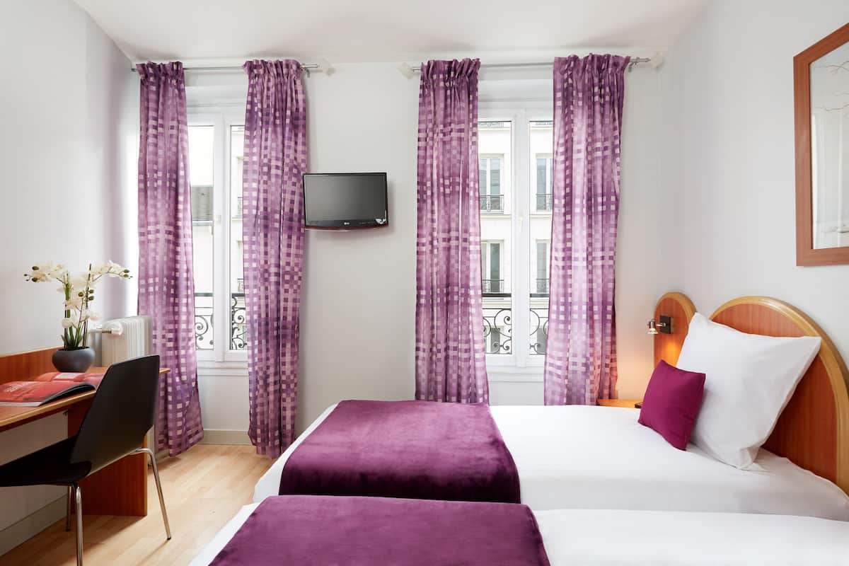 A hotel room with two beds, a desk, a chair, a TV, and a balcony view.