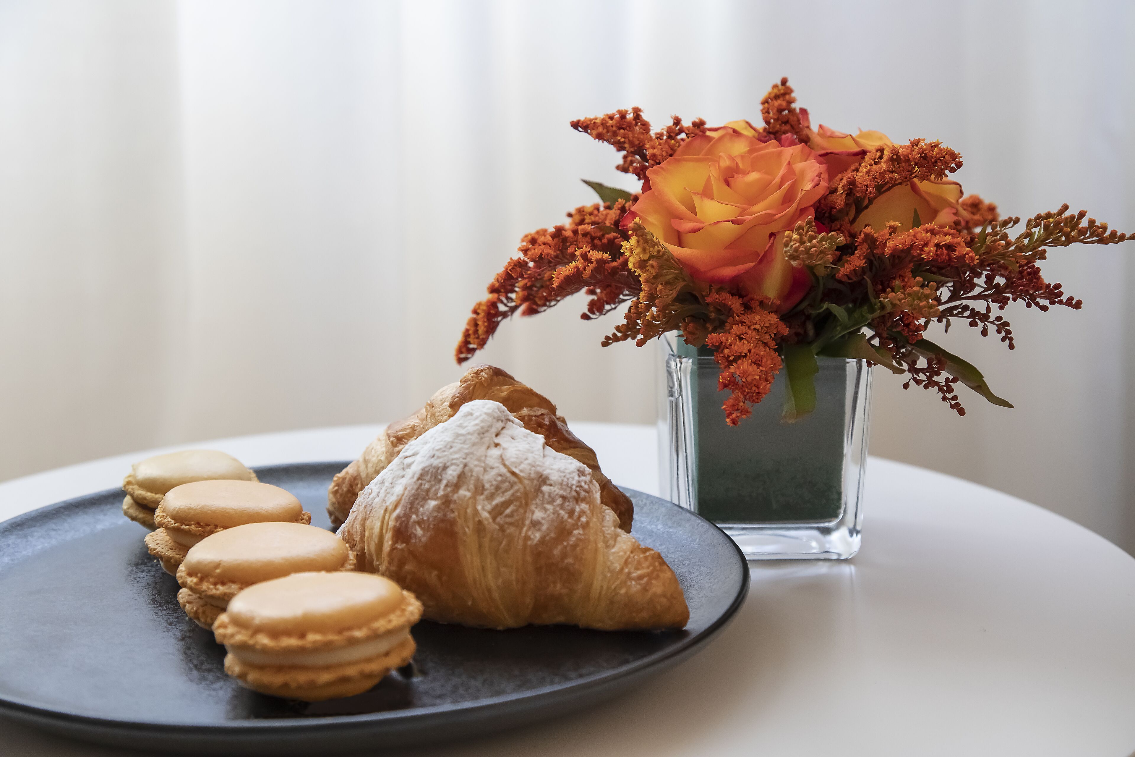 Un plato con macarons y un croissant, y un florero con flores.