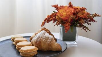 Un plato con macarons y un croissant, y un florero con flores.