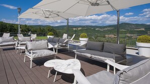 A deck with outdoor furniture, including sofas and chairs, under large umbrellas, overlooking a scenic landscape. - La Reggia Sporting Center (Cascia)