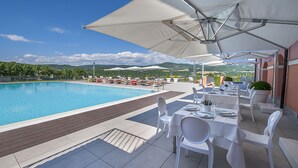 A poolside dining area with white tables and chairs, umbrellas, and a view of the pool and landscape. - La Reggia Sporting Center (Cascia)