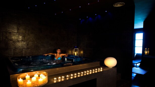 A dimly lit room with a hot tub, candles, and a person relaxing. - La Reggia Sporting Center (Cascia)
