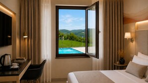 A hotel room with a bed, a desk, a chair, a TV, a window with a view of a pool and mountains, and a lamp. - La Reggia Sporting Center (Cascia)