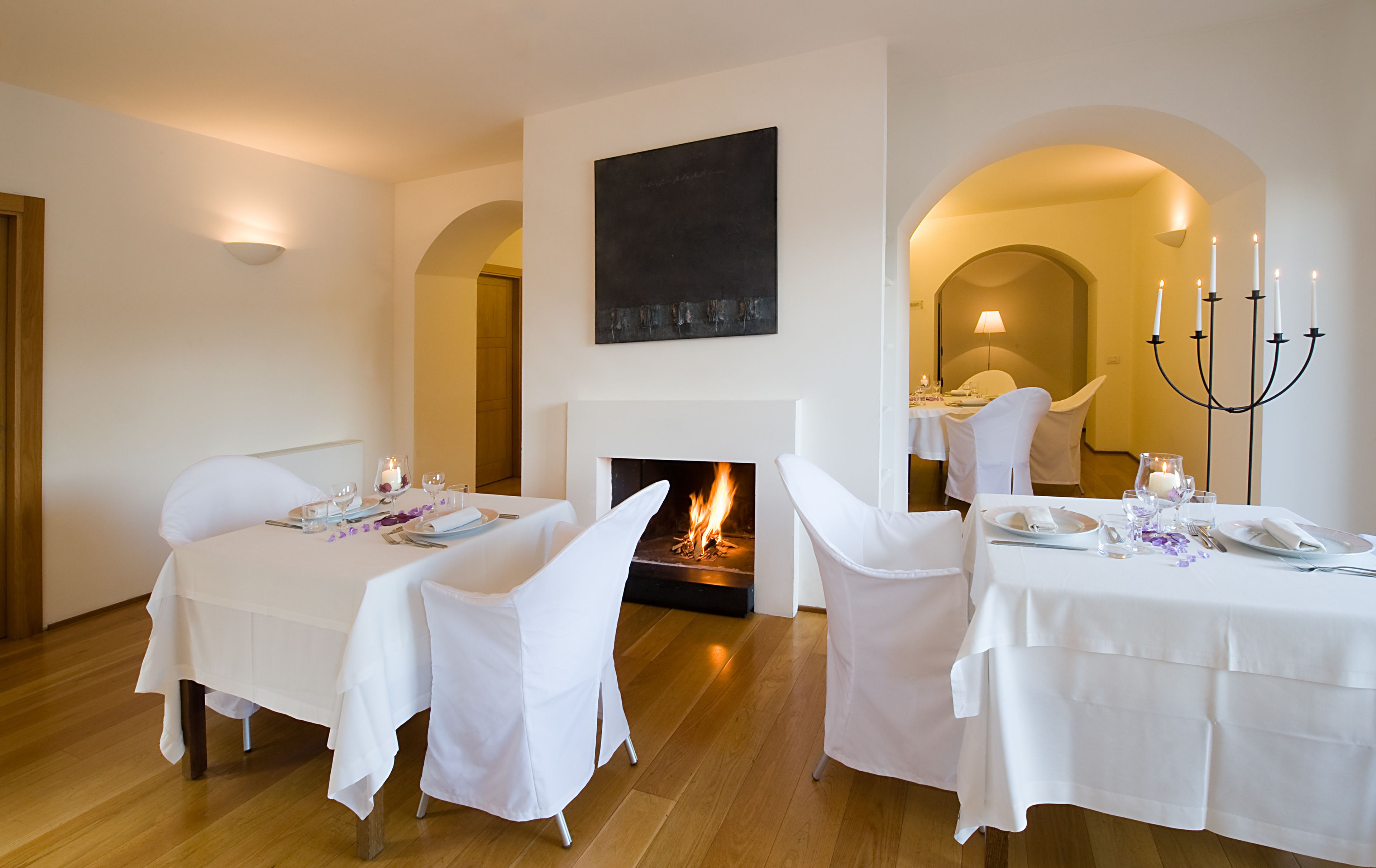 Un comedor con dos mesas dispuestas para una comida, una chimenea y un candelabro.