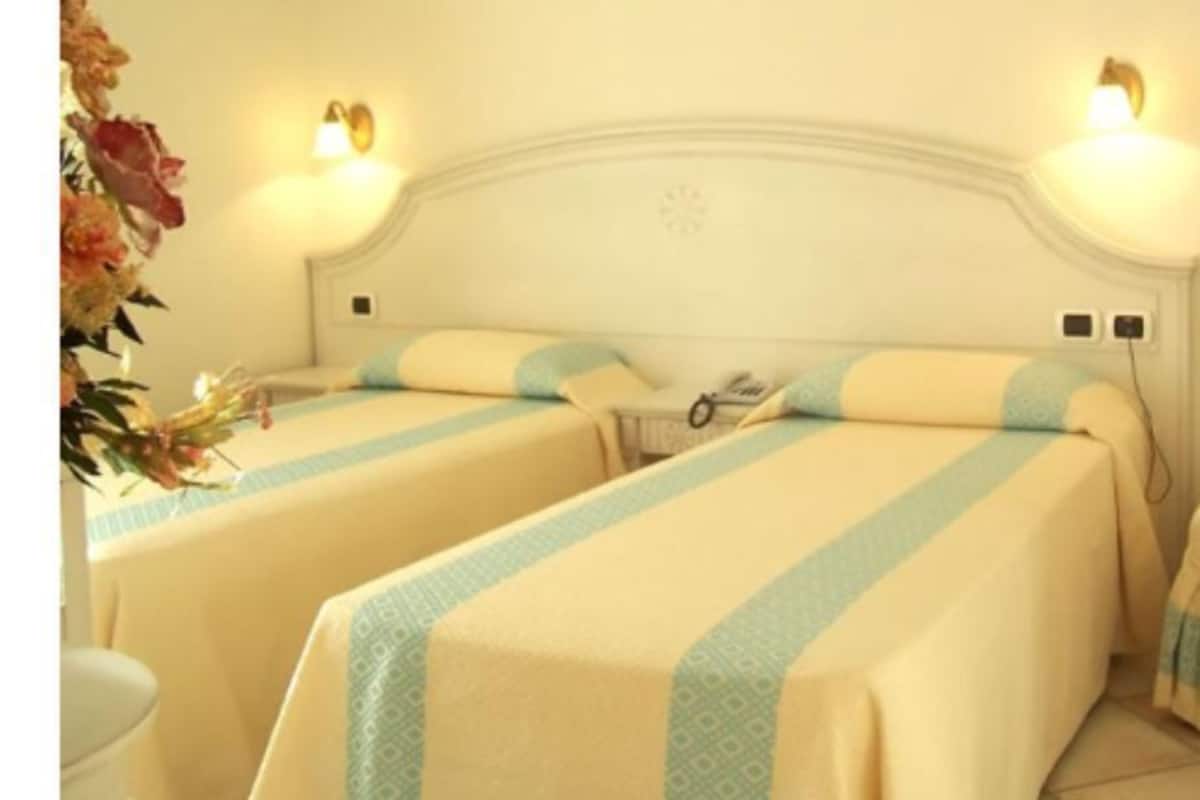 Une chambre d’hôtel avec deux lits, chacun recouvert d’une couvre-lit à rayures et agrémenté d’oreillers assortis. Des appliques murales sont fixées au-dessus des lits.