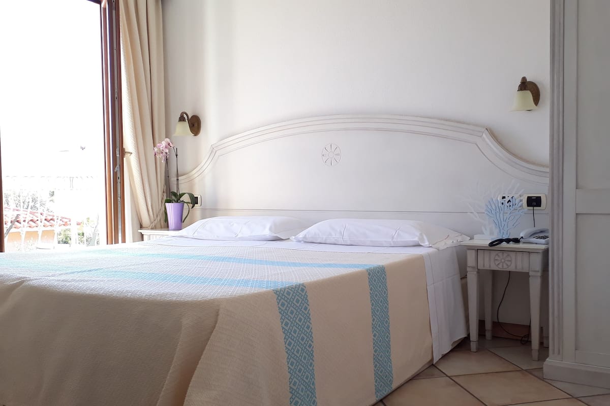 Un lit bien fait, avec du linge de lit blanc, une table de chevet avec une lampe et une horloge murale.