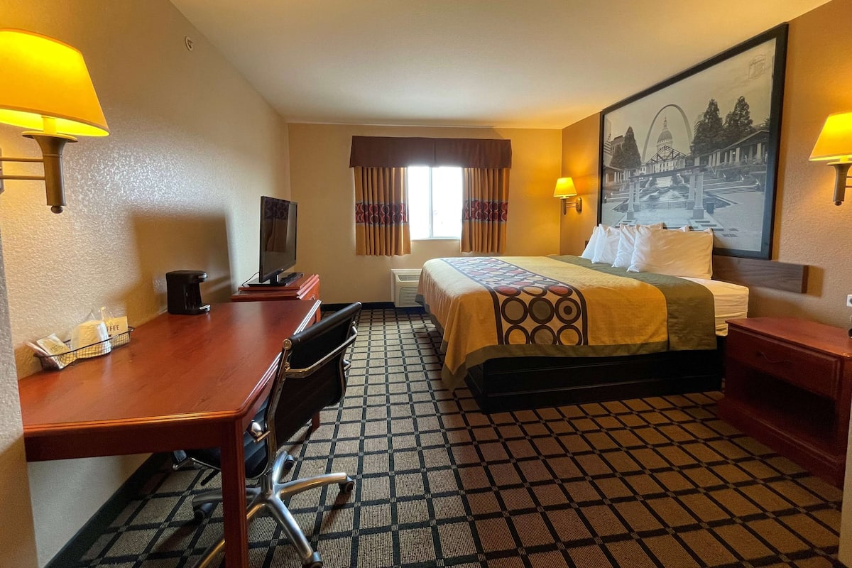 A hotel room with a bed, desk, chair, and a painting on the wall.
