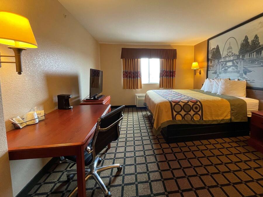 A hotel room with a bed, desk, chair, and a painting on the wall.