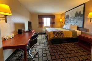 Una habitación de hotel con cama, escritorio, silla y un cuadro en la pared.