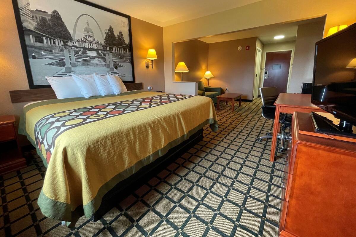 A hotel room with a bed, a television, a desk, a chair, and a lamp.