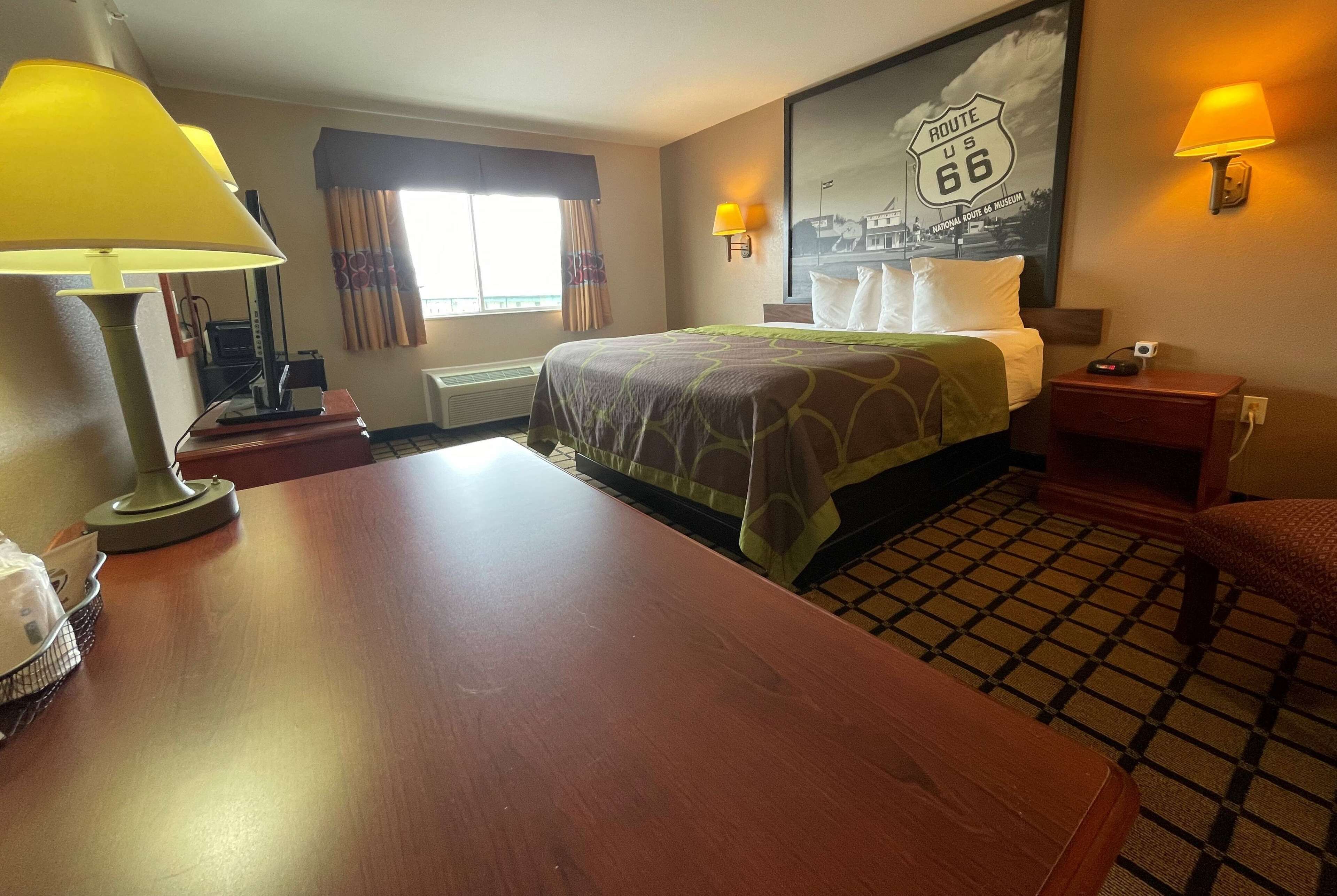 Une chambre d’hôtel comprenant un lit, un bureau, une lampe, une chaise, une fenêtre avec des rideaux, une lampe fixée au mur et une affiche de la Route 66.