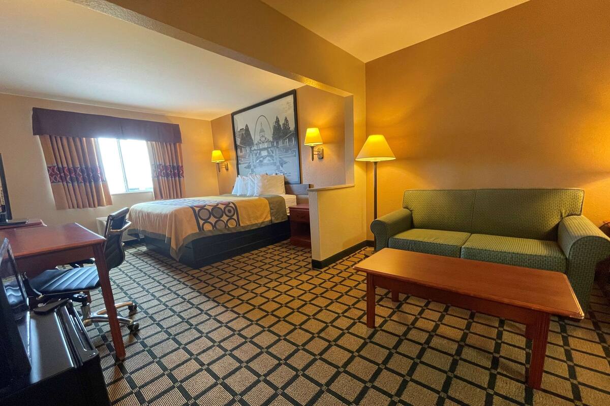 A hotel room with a bed, a desk, a chair, a sofa, and a lamp.
