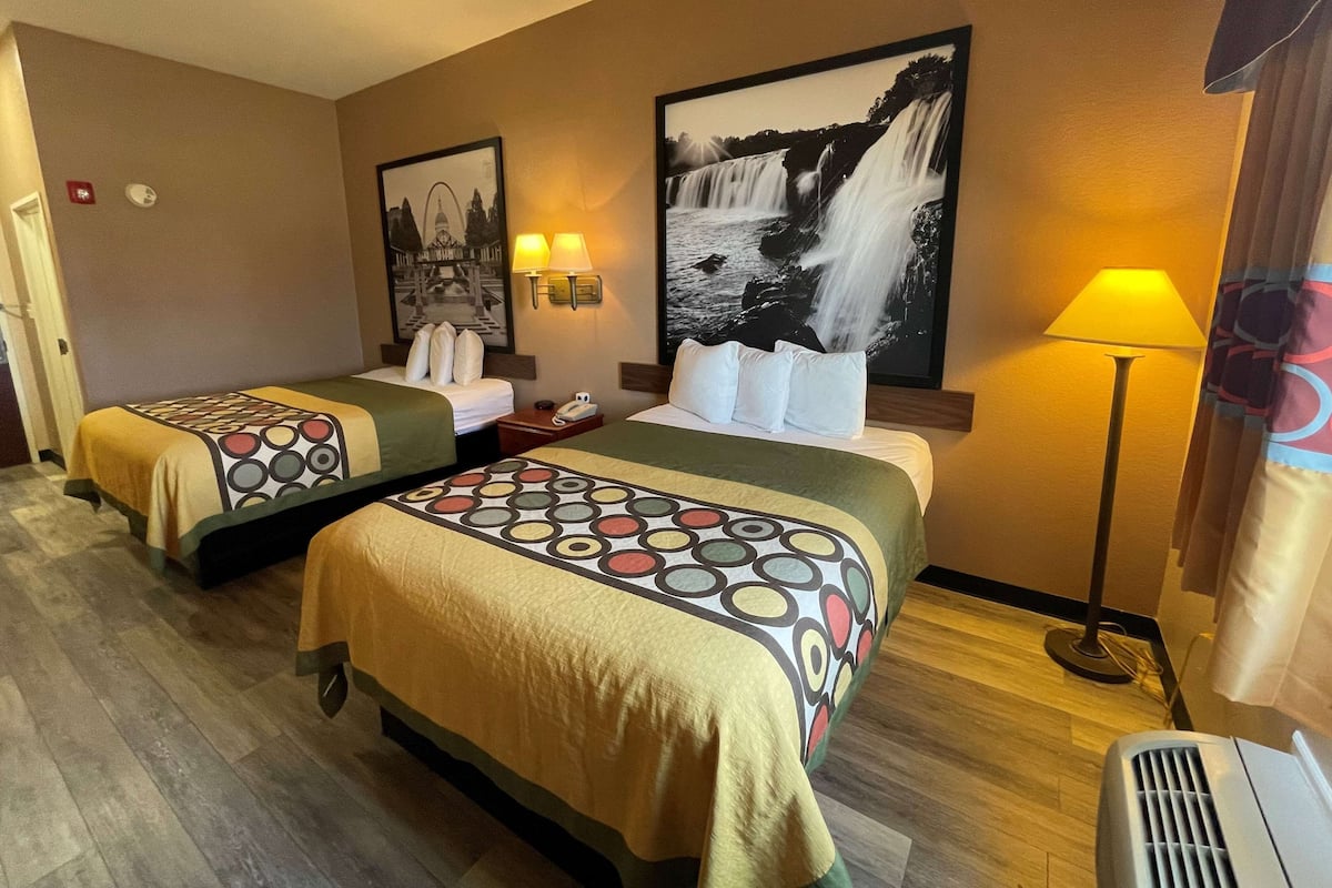 A hotel room with two beds, a large wall-mounted picture of a waterfall, a standing lamp, and a heater.