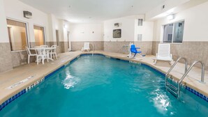 Una piscina interior con agua cristalina, sillones de descanso blancos y una silla azul.