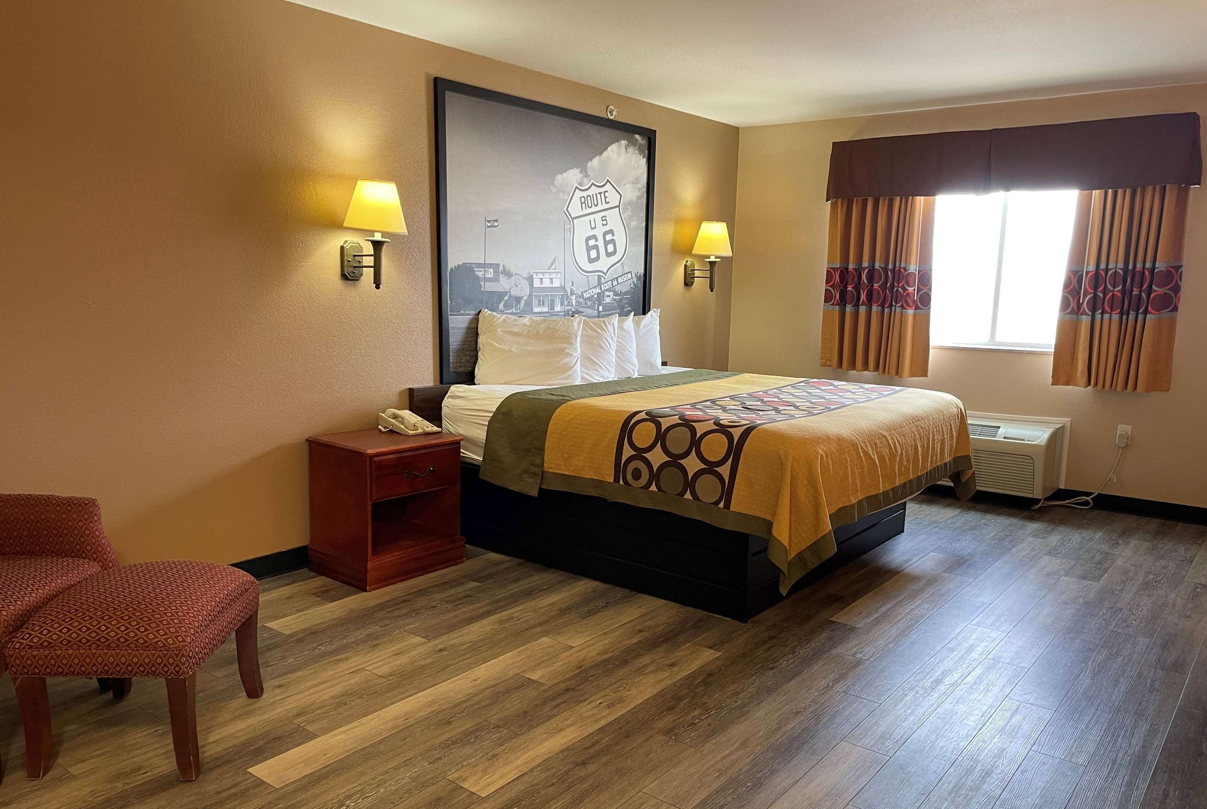 Ein Hotelzimmer mit einem großen Bett, zwei Nachttischlampen, einem Nachttisch, einem Sessel und einer Wand-Klimaanlage.