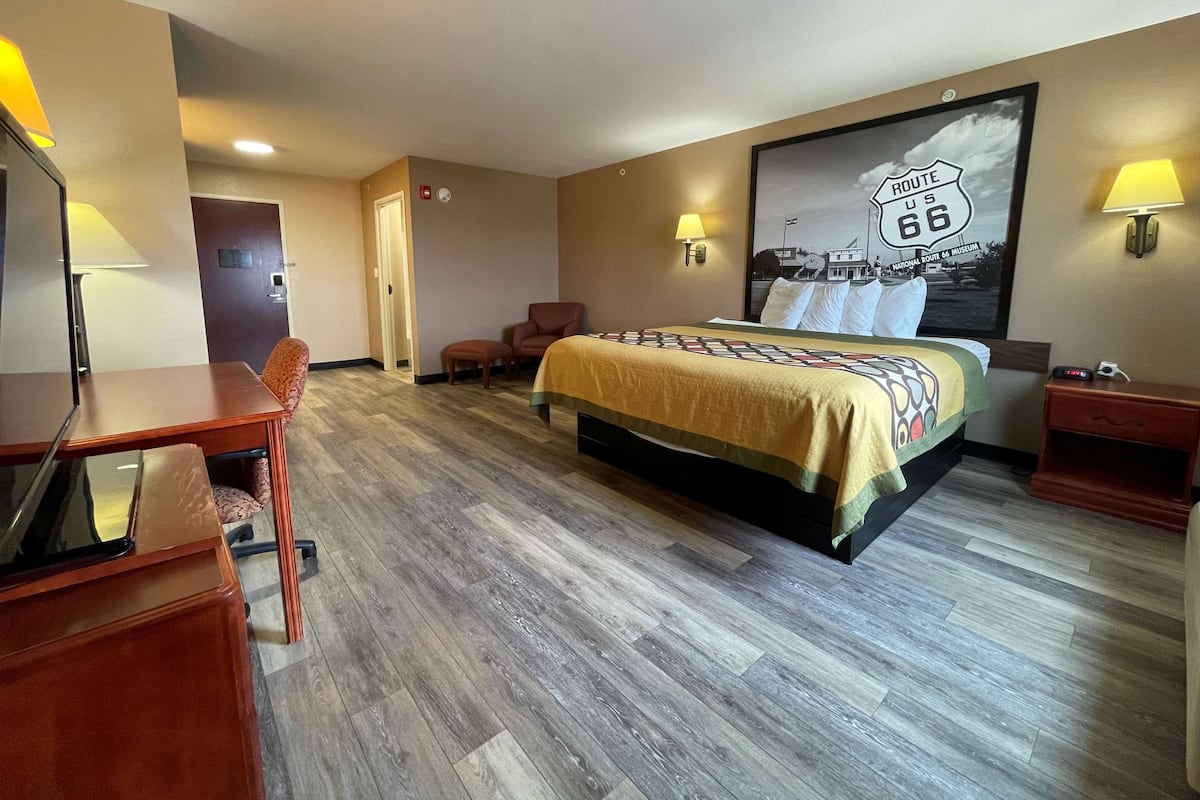 A hotel room with a large bed, a desk, a chair, a small table, and a lamp.