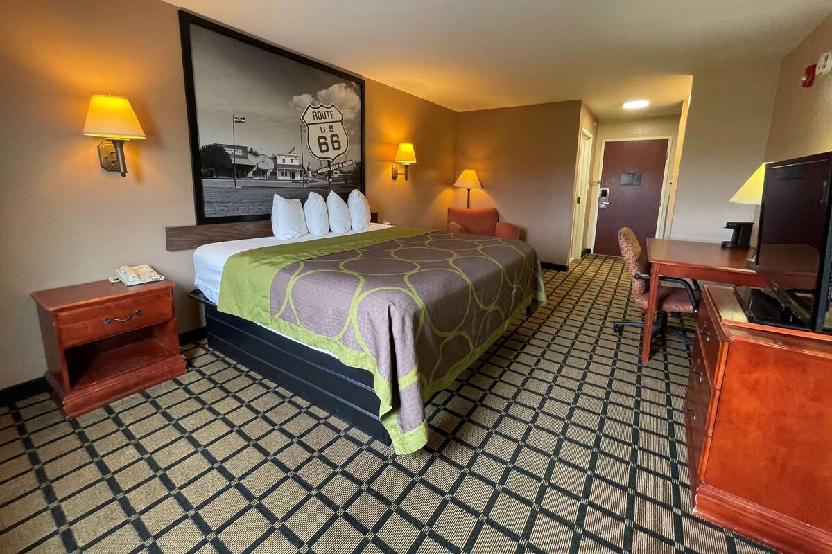A hotel room with a bed, two bedside tables, a desk, and a chair. There are two wall-mounted lamps and a large framed picture on the wall.