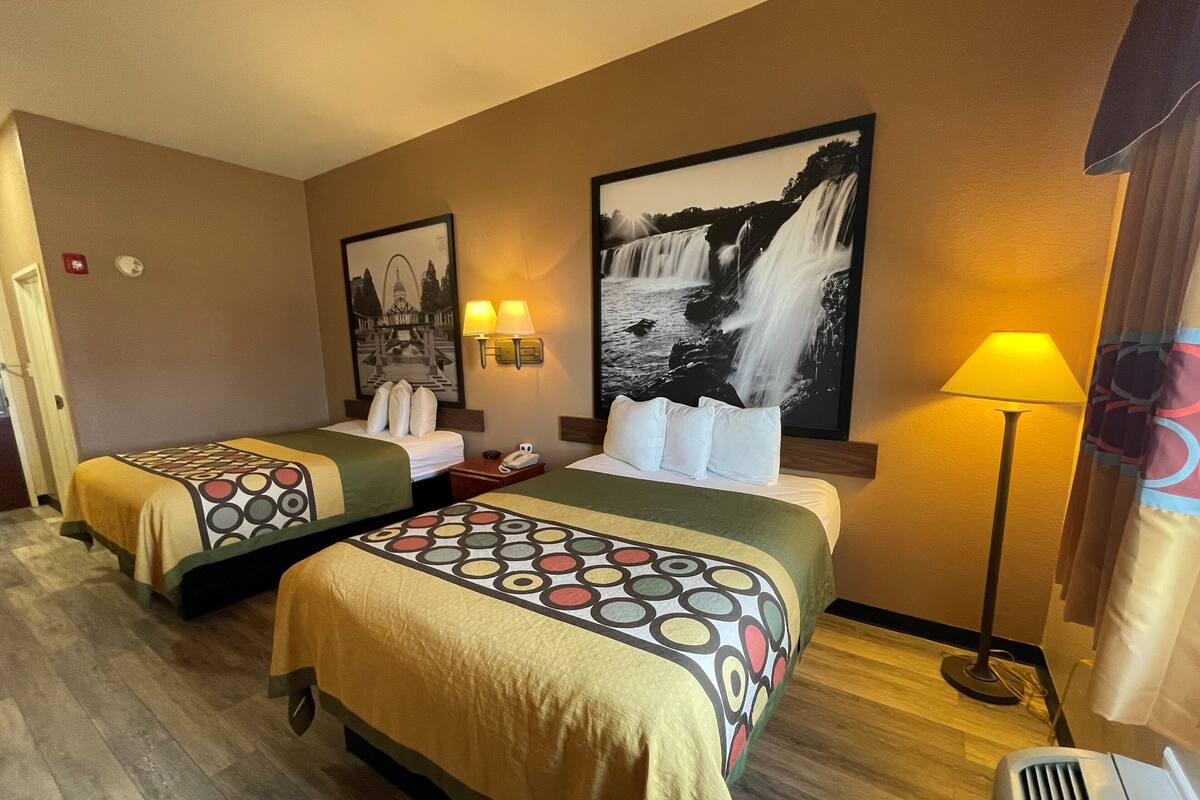 A hotel room with two beds, a large wall-mounted picture of a waterfall, a standing lamp, and a telephone on the nightstand.