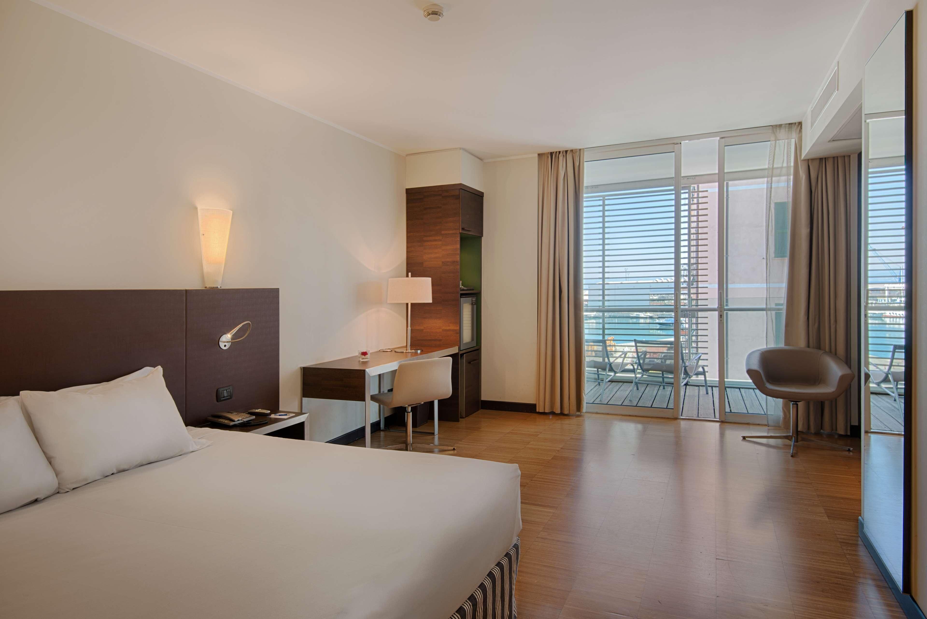 Une chambre d’hôtel avec un lit, un bureau, une chaise et un balcon offrant une vue.