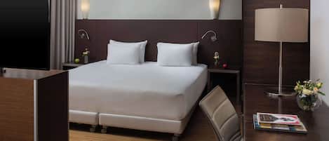 A hotel room with a large bed, a TV, a desk, a lamp, and a vase with flowers.