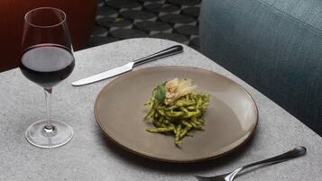Una mesa de comedor con un plato de pasta, una copa de vino y cubiertos.