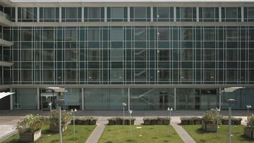 Un bâtiment moderne doté d’une façade en verre, d’une cour intérieure agrémentée de jardinières et surplombé d’un ciel dégagé.
