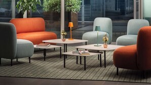A modern lounge area with seating and tables, large windows, and indoor plants.