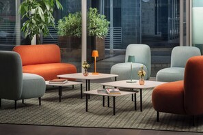 A modern lounge area with seating and tables, large windows, and indoor plants. - NH Savona Darsena (Savona)