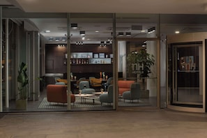 A modern hotel lobby with glass walls, comfortable seating, a bar area, and a visible plant. - NH Savona Darsena (Savona)