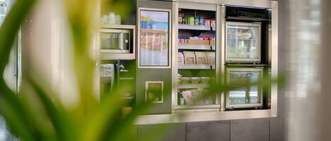 Um quiosque de autoatendimento com áreas refrigeradas, provavelmente para bebidas e lanches, em um ambiente moderno.