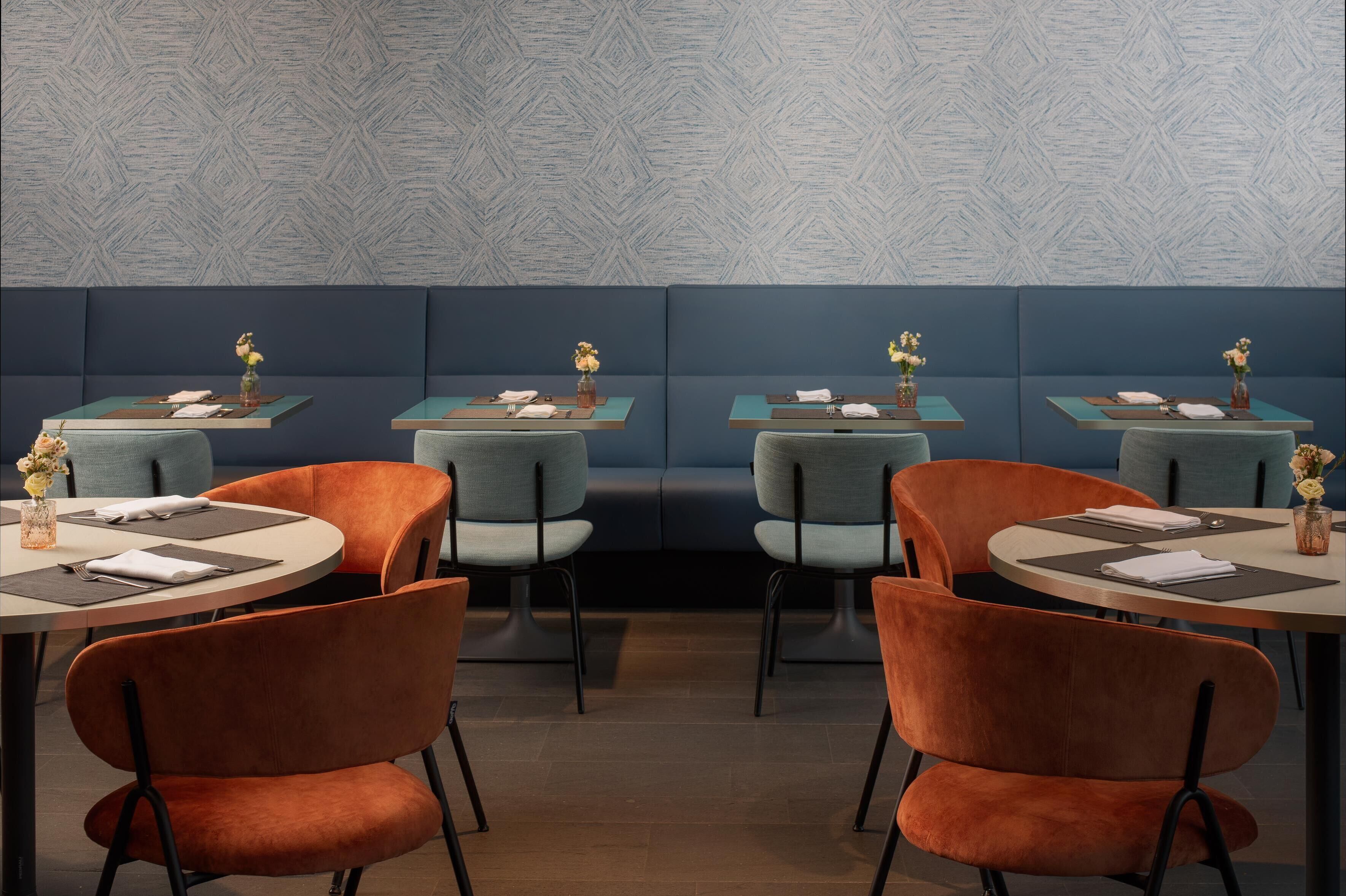 A restaurant with booths and round tables, each with a vase of flowers and a menu.