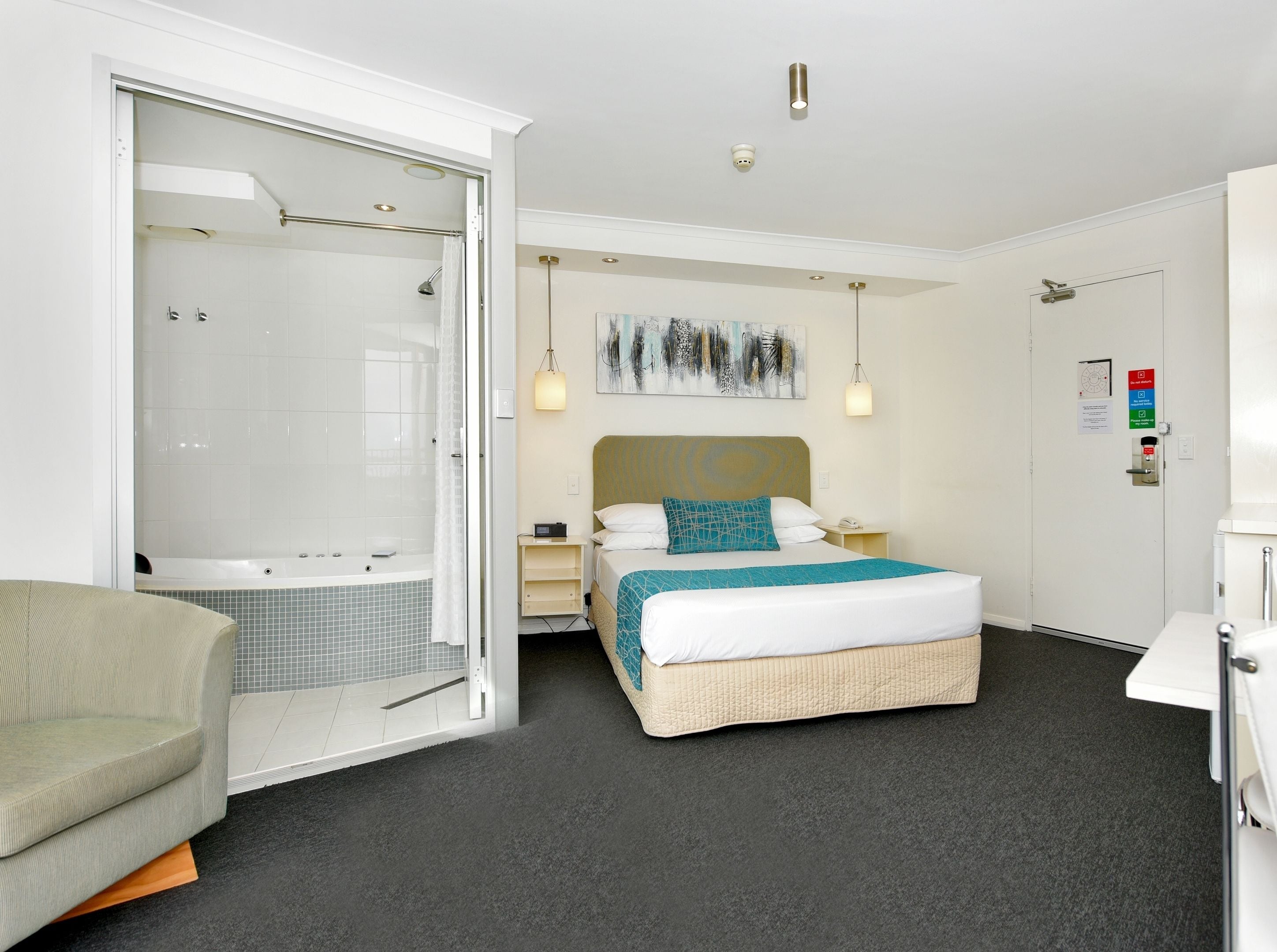Una habitación de hotel moderna con una cama grande, una zona de ducha separada, una mesita de noche pequeña y una silla.