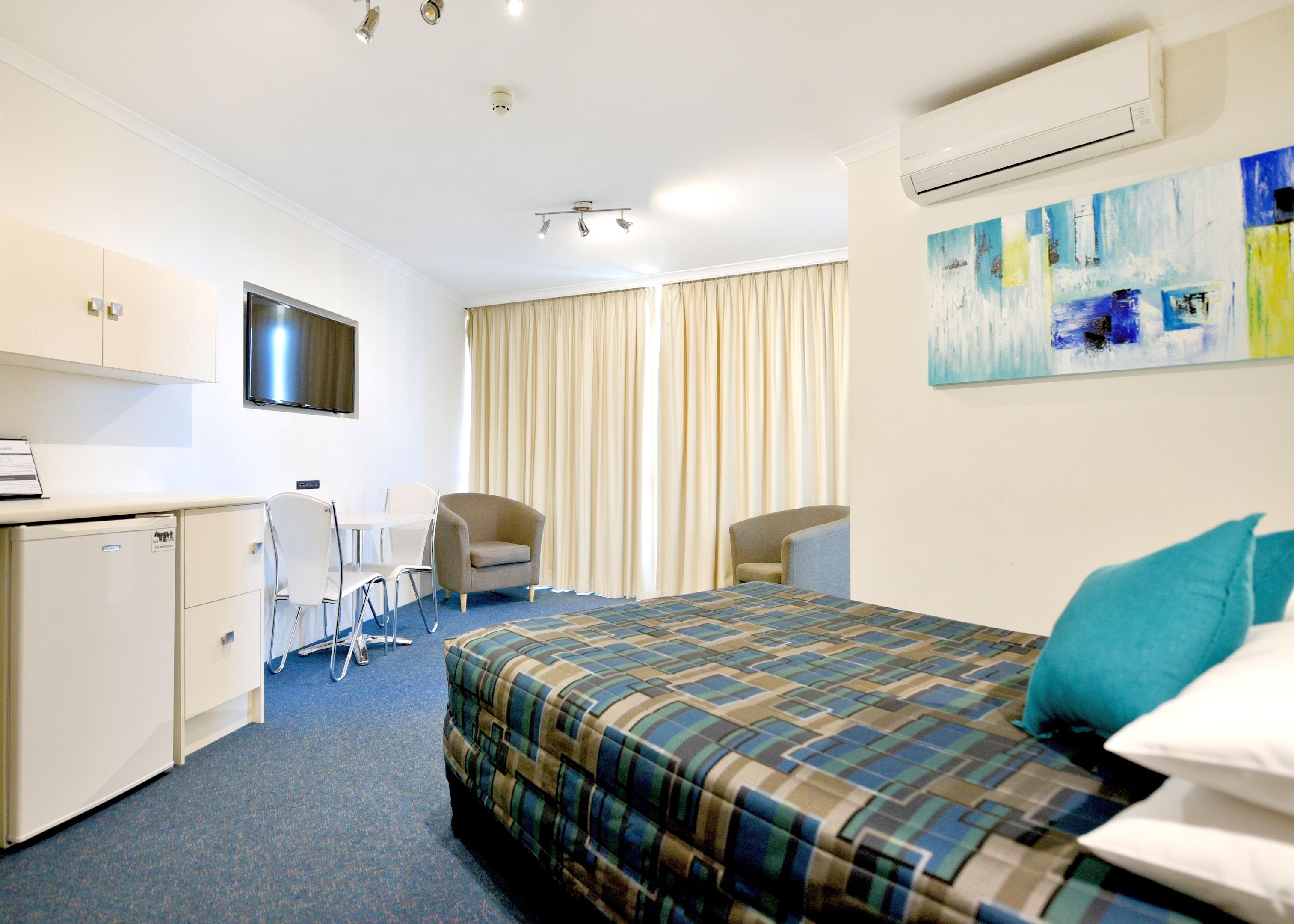 A hotel room with a bed, a desk, a chair, a TV, and an air conditioner.
