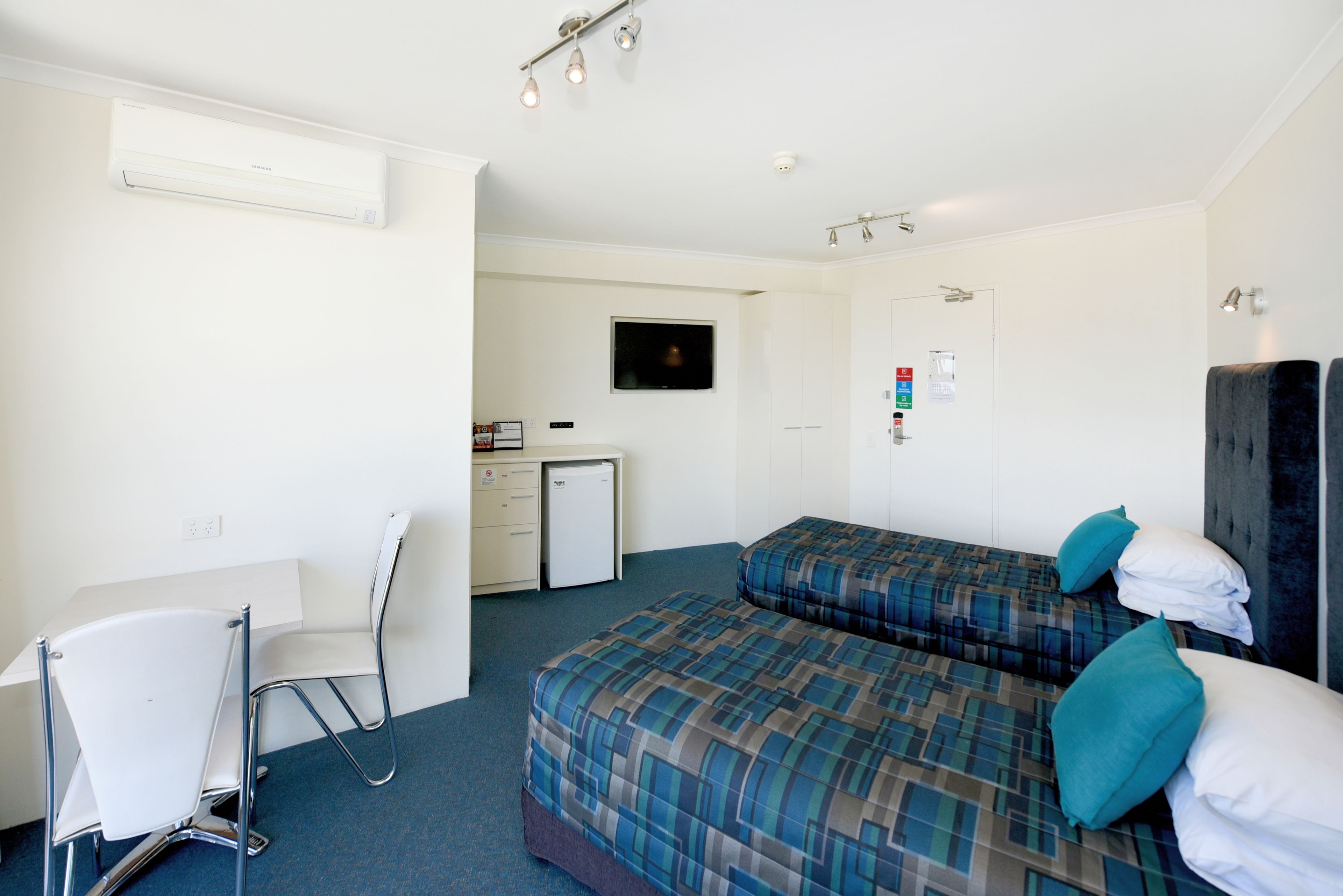 A hotel room with a bed, a desk, a chair, a television, and a small kitchenette.