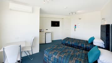 A hotel room with a bed, a desk, a chair, a television, and a small kitchenette.