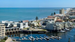 A marina with boats docked, surrounded by modern buildings and a clear view of the ocean.