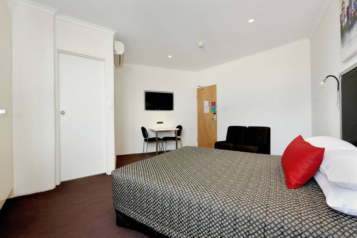 Ett hotellrum med en säng, ett skrivbord, en stol, en tv och en dörr.