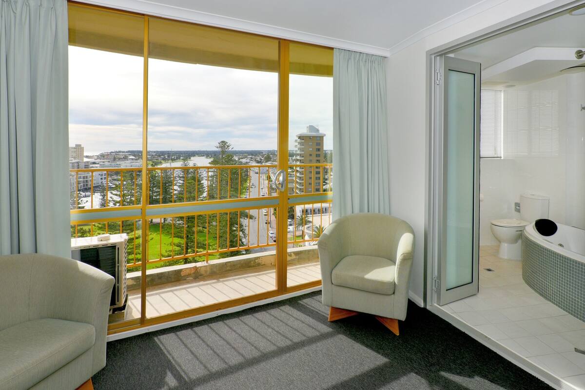Ett hotellrum med en balkong, en soffa, en fåtölj, ett badkar och en toalett.