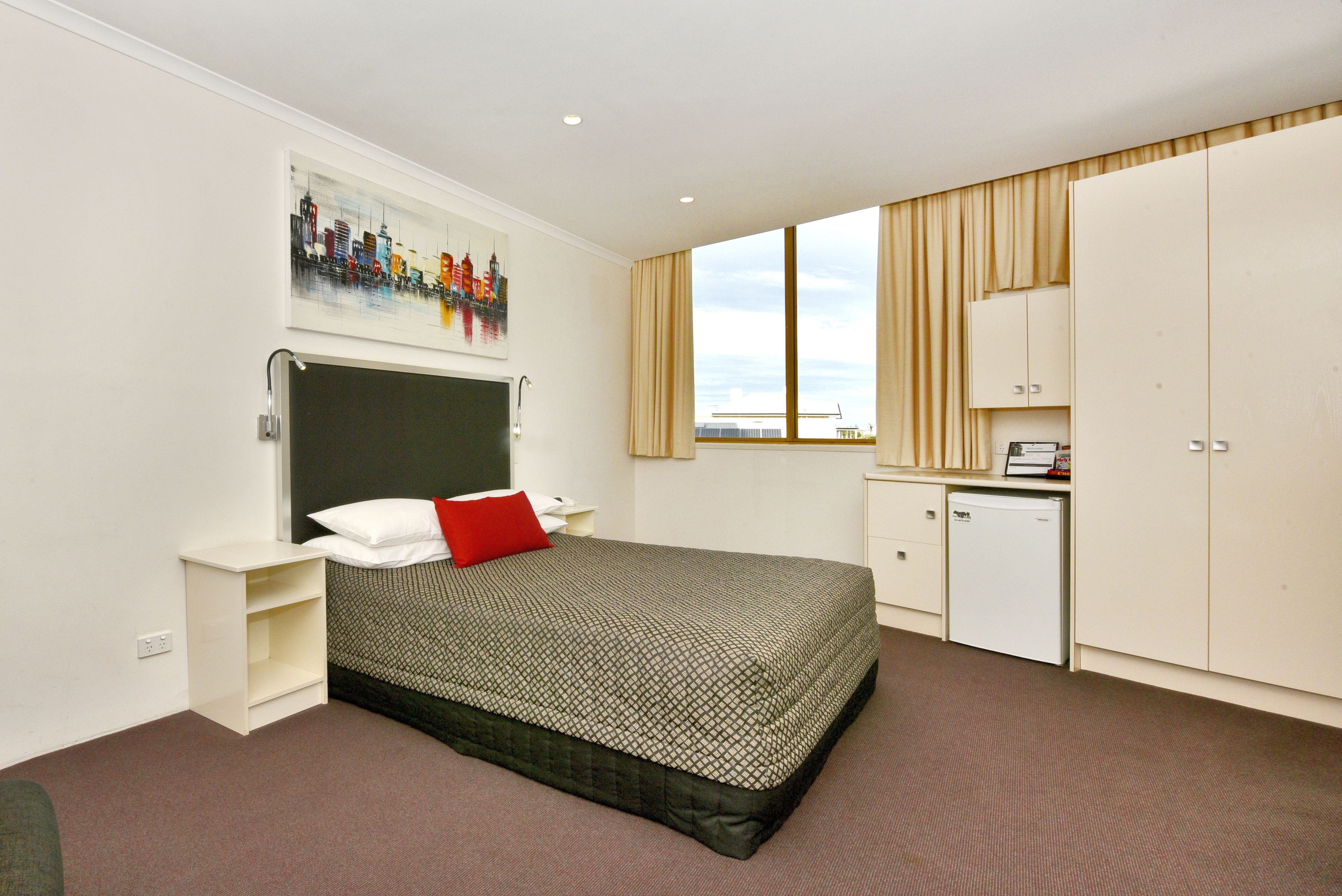 Habitación de hotel con cama, mesita de noche, escritorio con computadora, armario y ventana con cortinas.