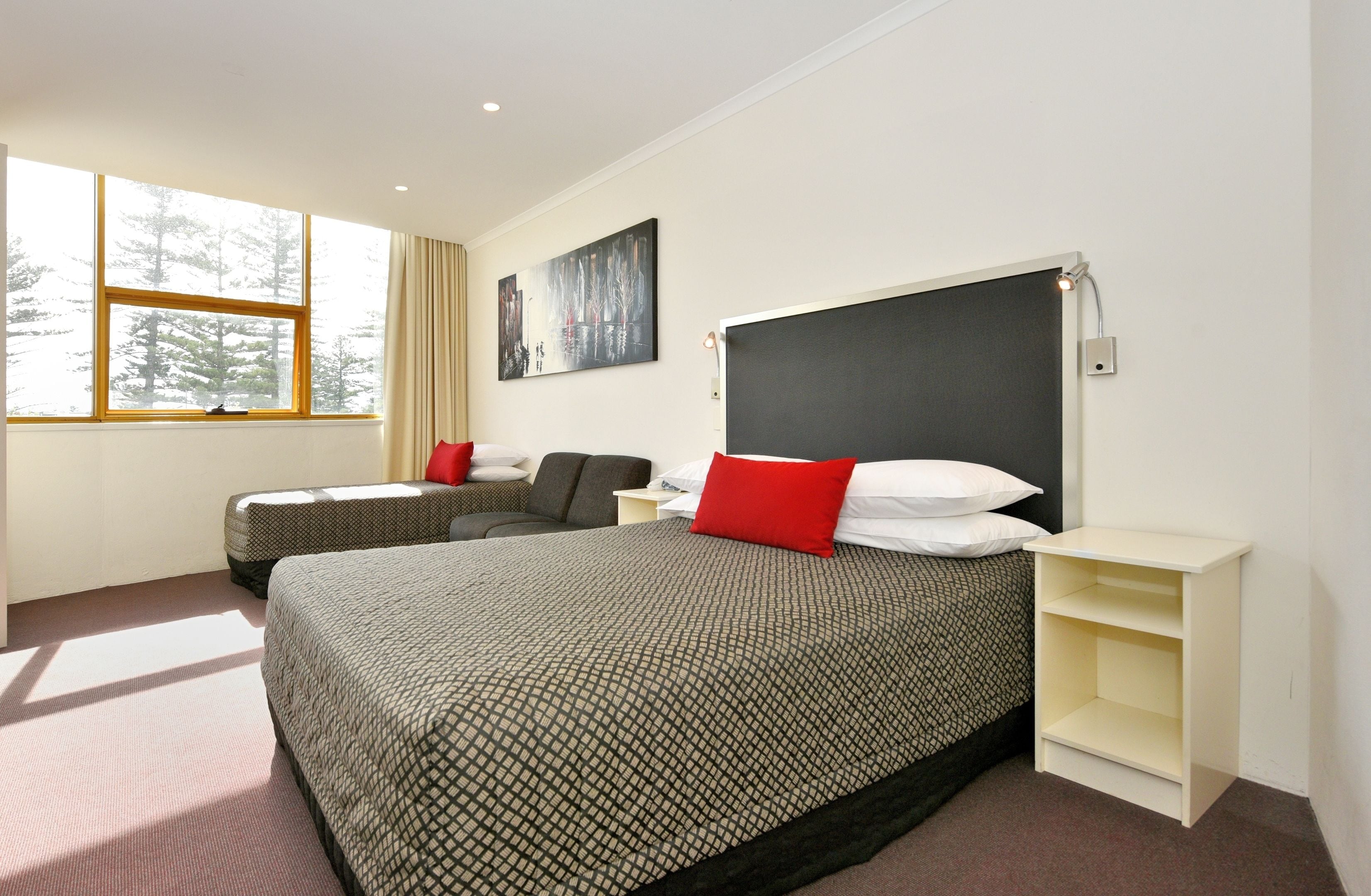 A hotel room with a large bed, a smaller bed, a desk, and a window with a view of trees.