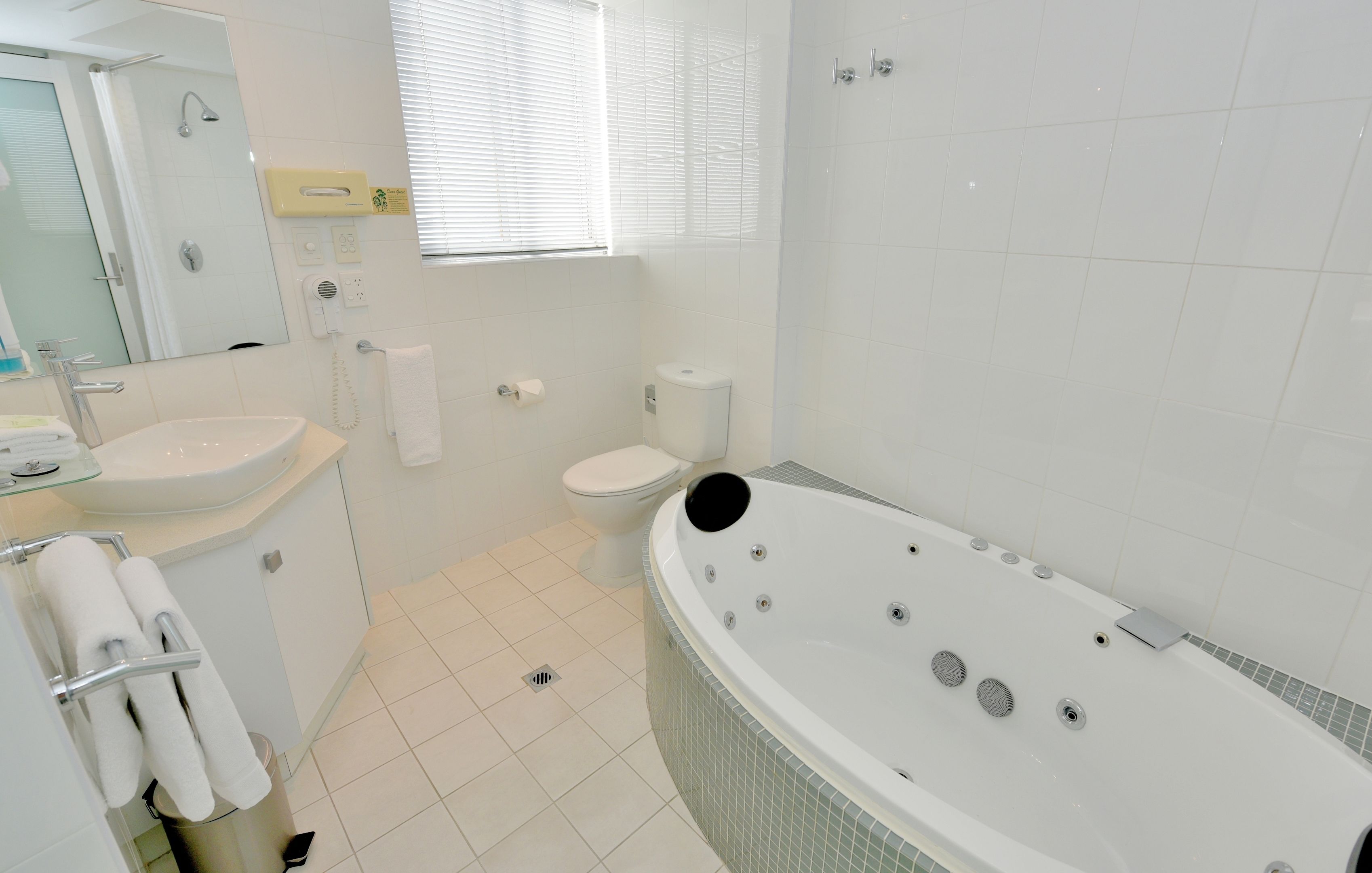 A modern bathroom with a large bathtub, a sink, a toilet, and a mirror.