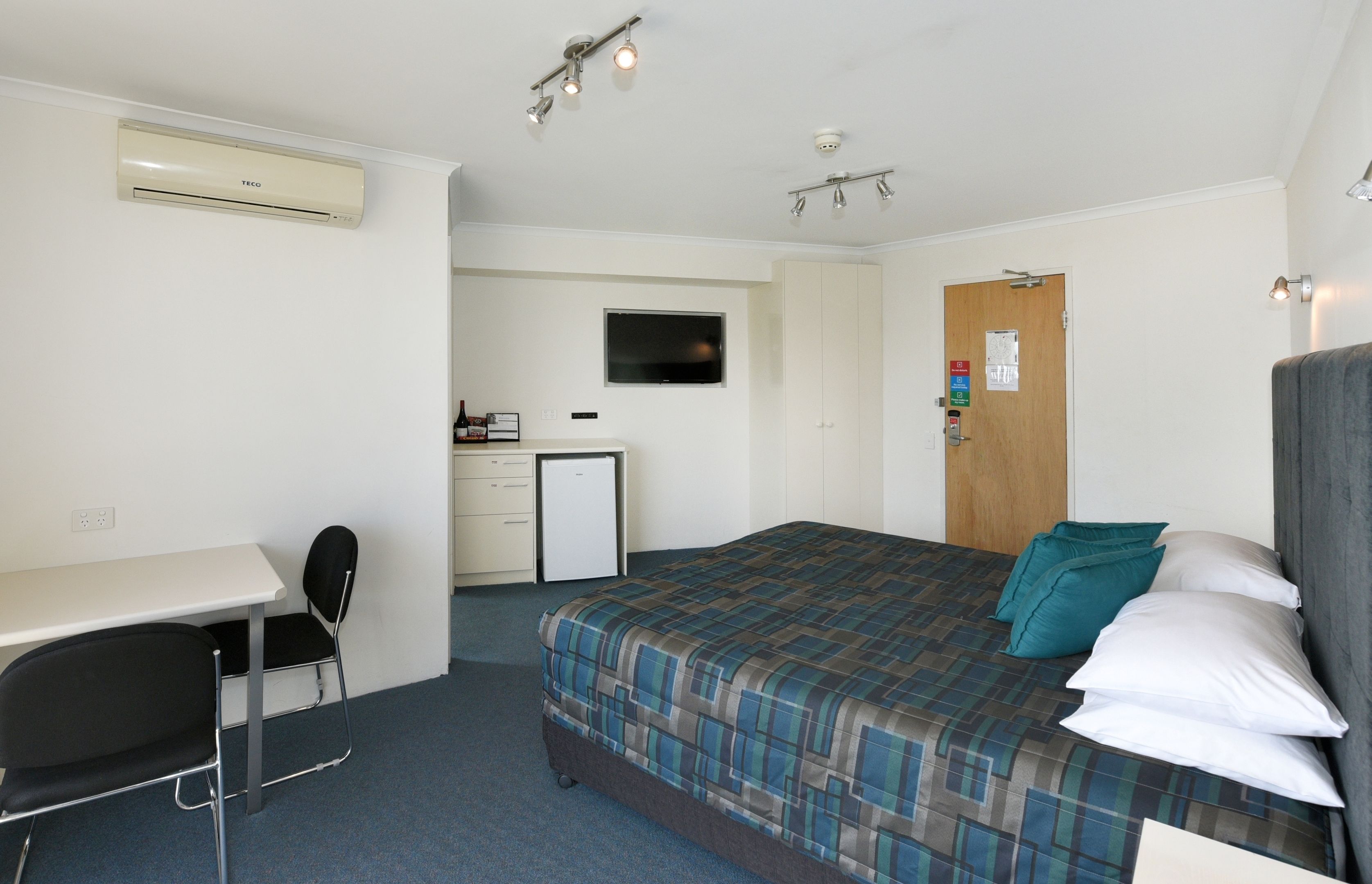 A hotel room with a bed, a desk, a chair, a television, and a door.