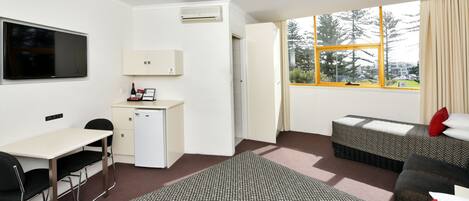 A hotel room with a desk, a small refrigerator, a TV, two beds, and a window with a view of trees.