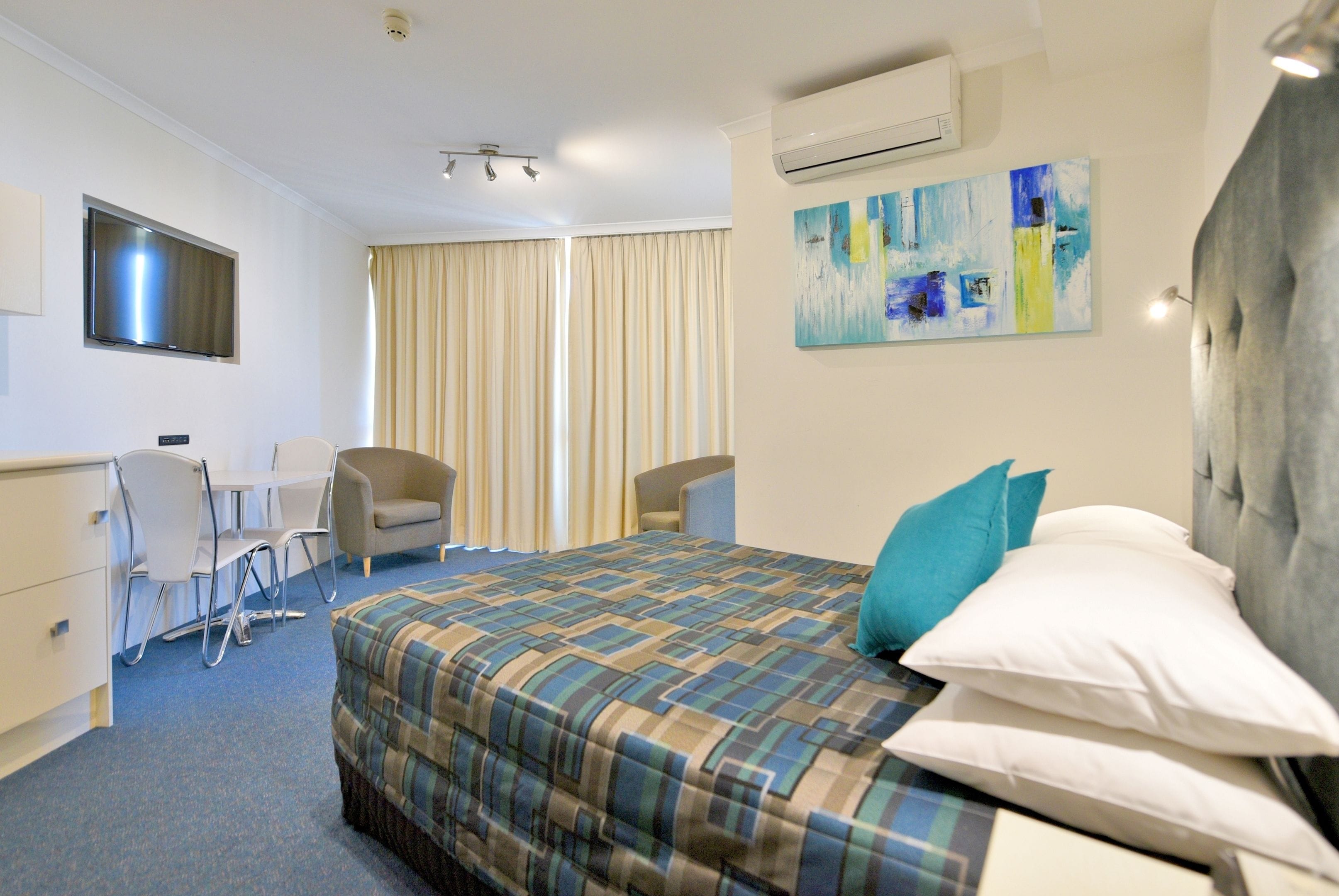 Une chambre d’hôtel avec un lit, deux chaises, un bureau et un téléviseur.