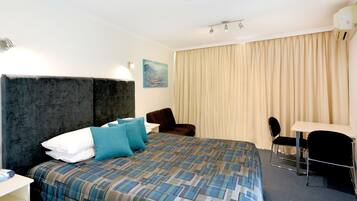 A hotel room with a large bed, a desk, a chair, and a window with curtains.